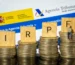 Bloques con letras IRPF sobre pilas de monedas junto al logo de la Agencia Tributaria
